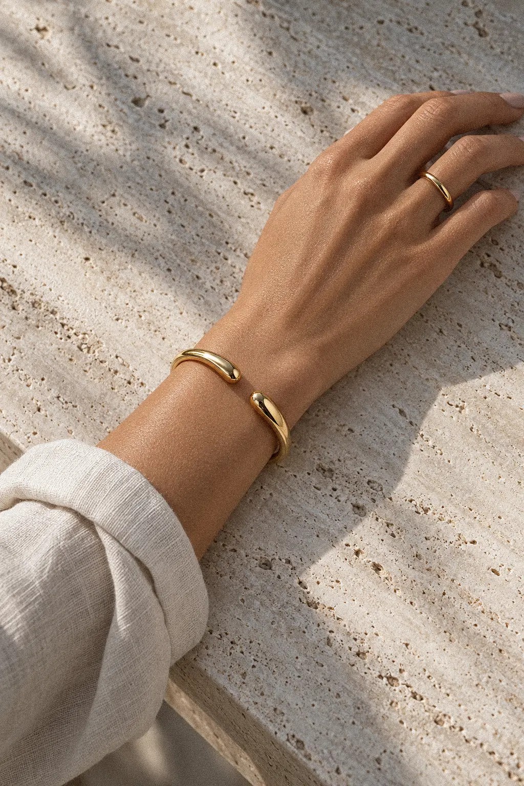 Wrist with a gold bangle on a sunlit stone surface